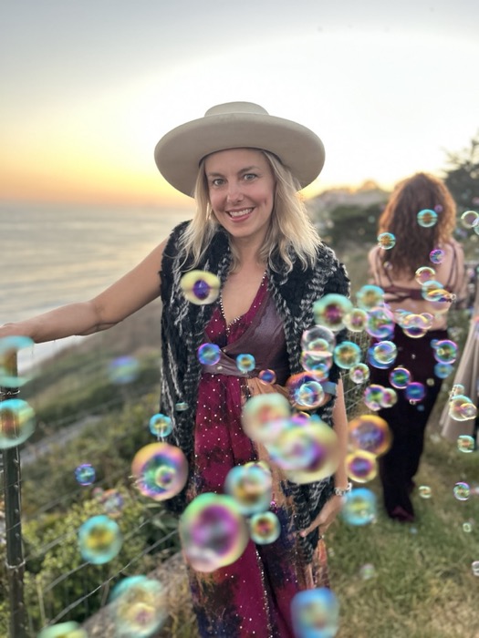 Maura at a sunset cliff amid drifting bubbles