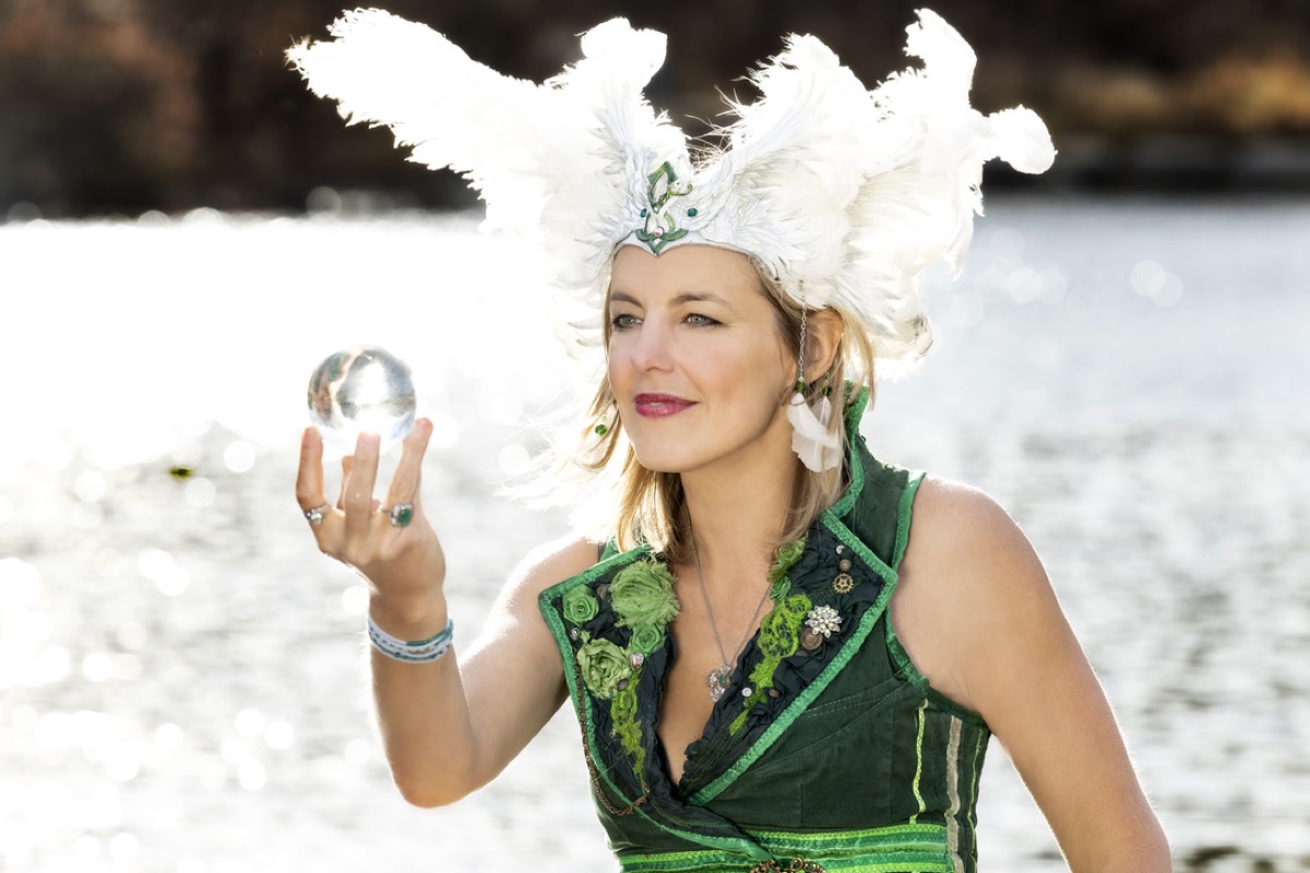 Maura in a white feather headdress seated over a sparkling lake